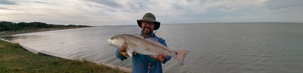 Matthew Bey pictures holding a Red Drum on the shore of Matagorda Bay in Texas